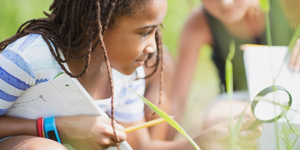 Two children exploring nature with a magnifying glass and notebooks outdoors.