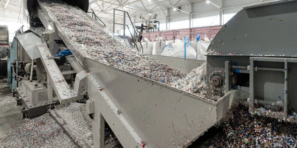 Industrial conveyor belt carrying shredded plastic inside a recycling plant.
