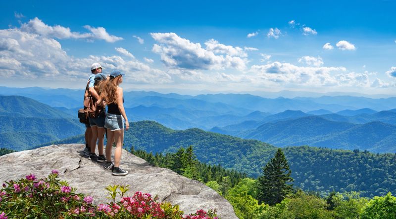 Family standing with arms around on top of the mountain, looking at beautiful summer mountains landscape. People hiking on vacation, enjoying beautiful view. Great Smoky Mountains in the background. Near Asheaville, North Carolina, USA.