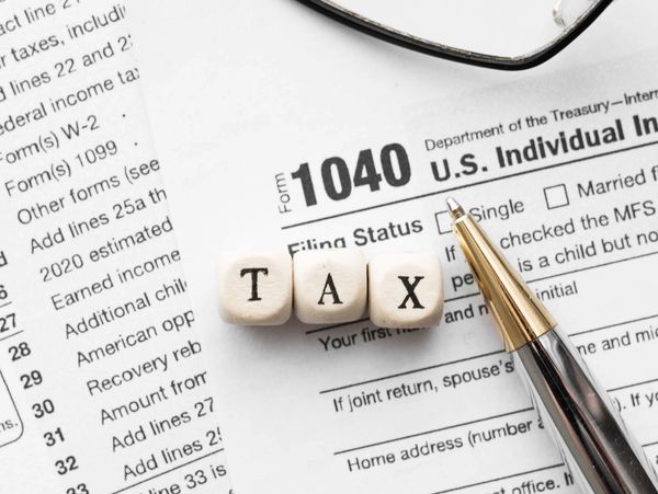Wooden blocks spelling TAX on a 1040 U.S. Individual Income Tax form with a pen.