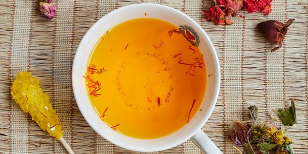 A cup of saffron tea with dried flowers and rock sugar on a woven mat.