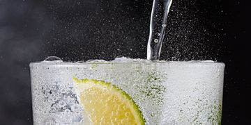 Close-up of sparkling water being poured with lime slices in a glass.
