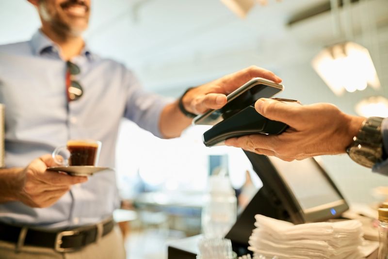 Cropped shot of a customer paying for coffee with a smartphone at a cafe