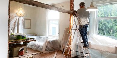 Man cutting metal beam in a room renovation with protective glasses and ladder.
