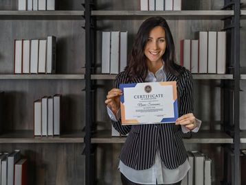 Smiling woman holding a certificate of appreciation in front of bookshelves.