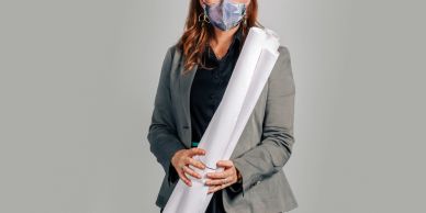 Woman in a mask holding rolled architectural plans.