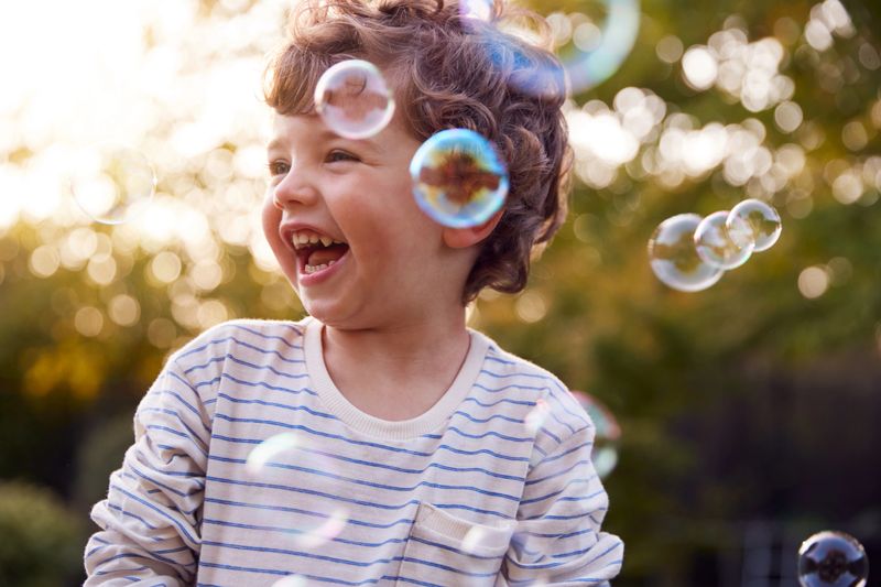 A joyful child laughing while blowing bubbles in a sunlit park.