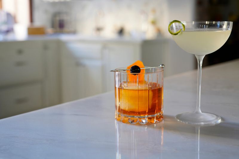 Pairing of old fashioned with an orange peel and cherry, and gimlet with a twist in a posh kitchen