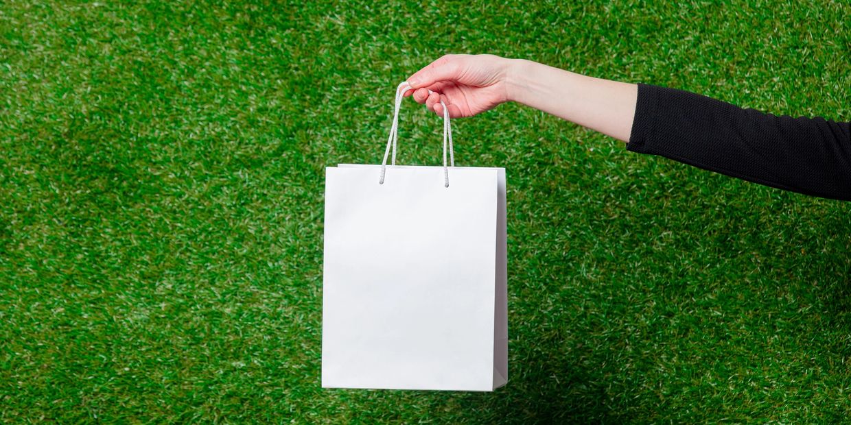 Hand holding a white paper bag against a green grass background.