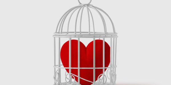 A red heart trapped inside a white birdcage symbolizing confined love.