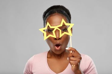 Woman holding star-shaped glasses with an surprised expression.