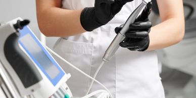 Person wearing black gloves holding a dental tool near a dental machine.