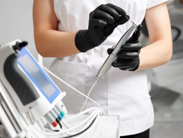 Person wearing black gloves holding a dental tool near a dental machine.