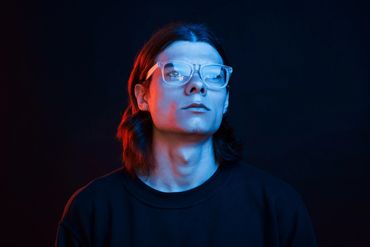 Young man with glasses in blue and red lighting.