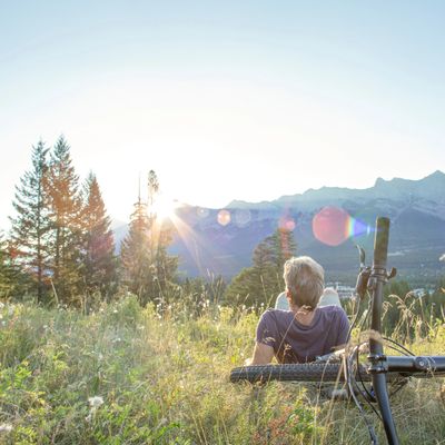 Person resting on grass with bicycle, watching the sunrise over mountains.
