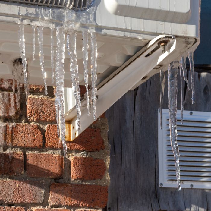 Icicles hanging from an outdoor air conditioning unit on a brick wall.