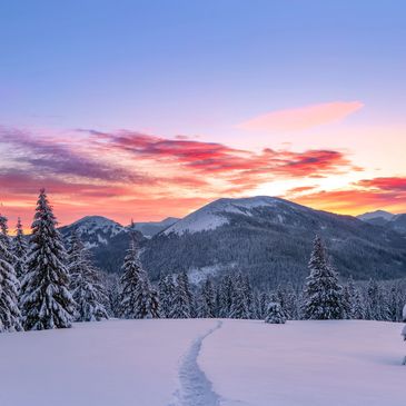 Snow-covered mountain landscape at sunset with a path through the snow.