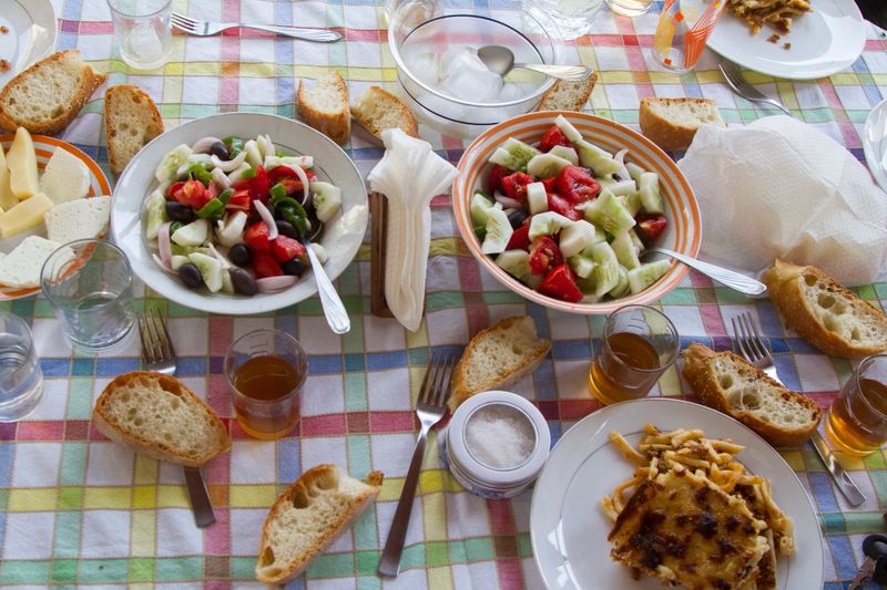 Naxos, Cyclades, Greece    Sunday table with Naxos products, bread, greek salad, gruyere, pastitsio and white wine.in a cart, colored tablecloth