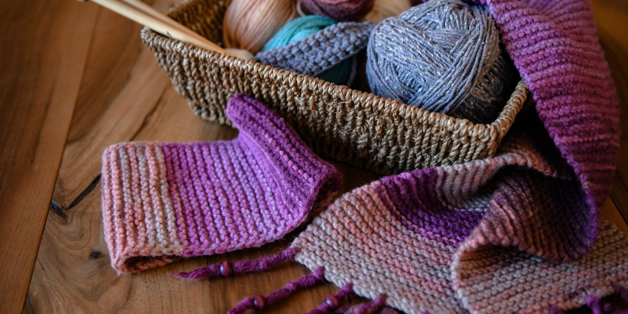 Écharpe tricotée violette avec pelotes de laine dans un panier.
