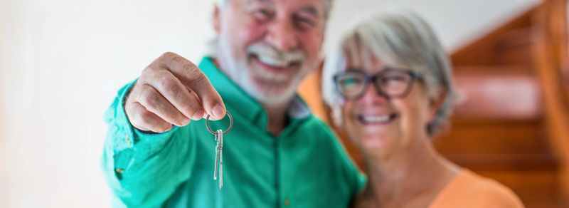 portrait and close up of two happy seniors buying a new house holding the key with his hand