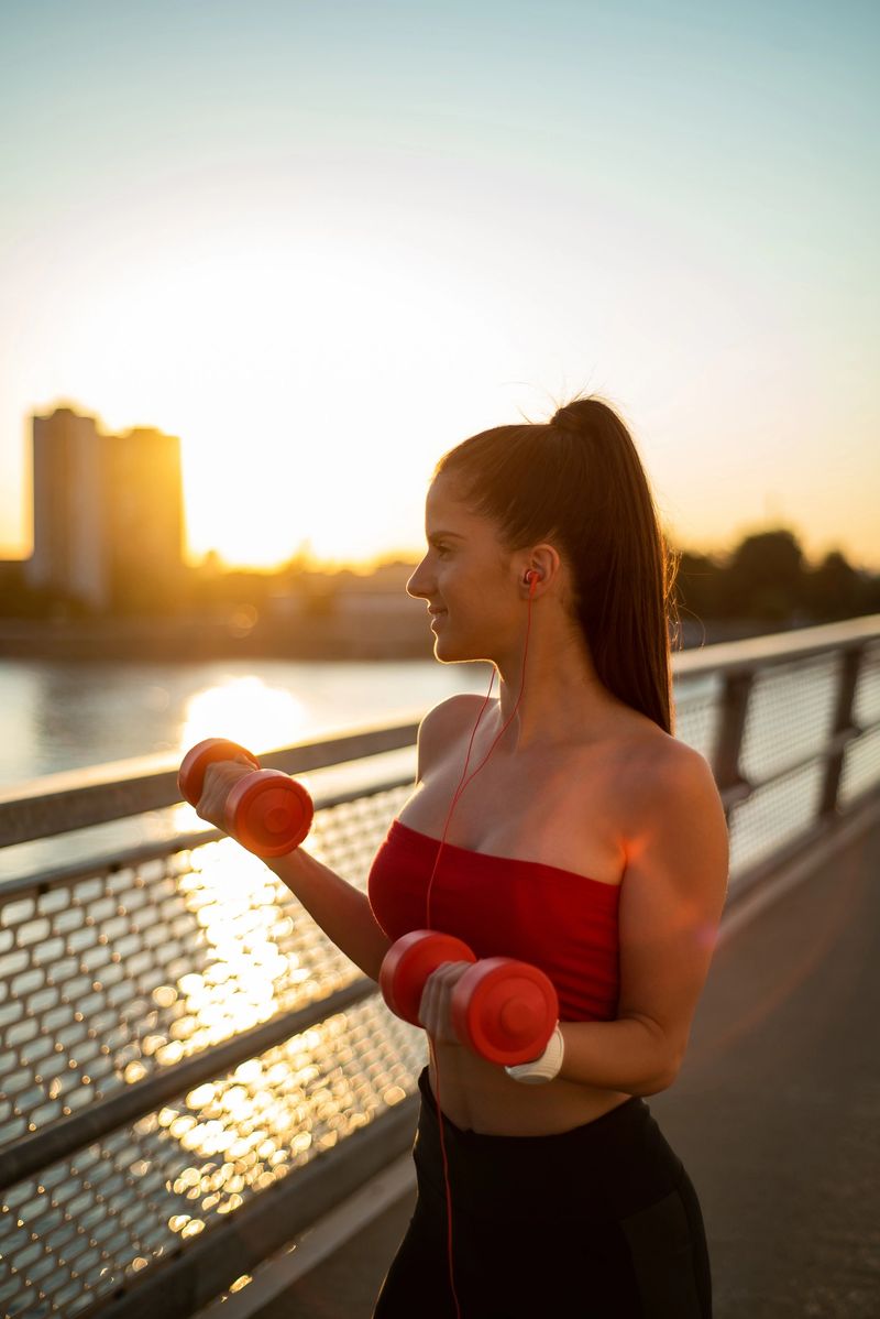 Cropped shot of young woman exercising with dumbbells outside in the morning sun while standing on a bridge