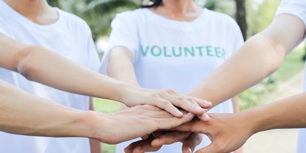 Volunteers joining hands in a show of unity and teamwork outdoors.