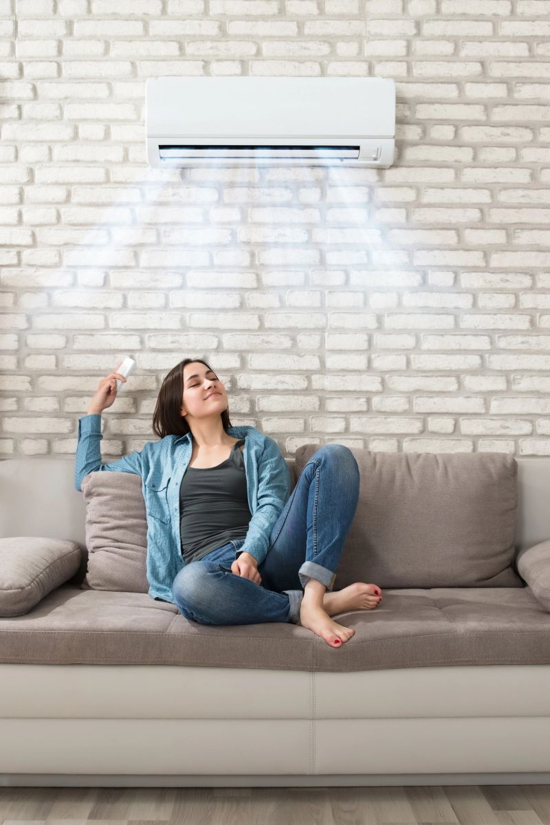 Happy Young Woman Holding Remote Control Relaxing Under The Air Conditioner