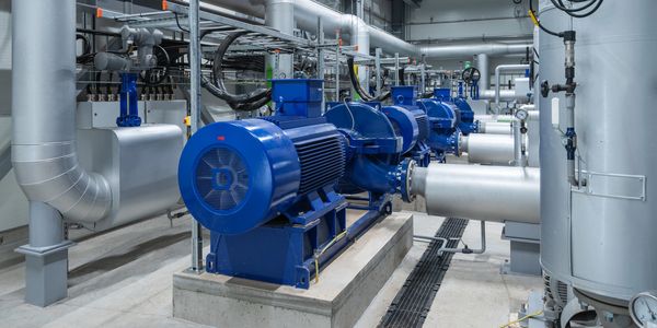 Industrial blue pumps and silver pipes in a clean mechanical room.