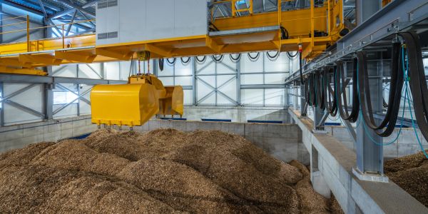 Grúa amarilla sobre montones de aserrín en almacén industrial.