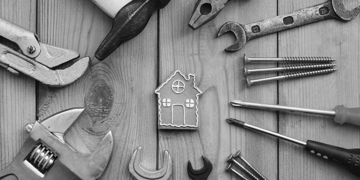 Tools surrounding a house-shaped cookie on a wooden surface.
