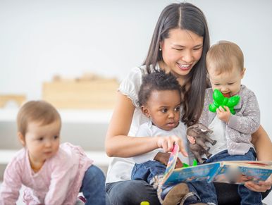 The picture shows a caregiver sitting with three young children in a bright and welcoming setting. 
