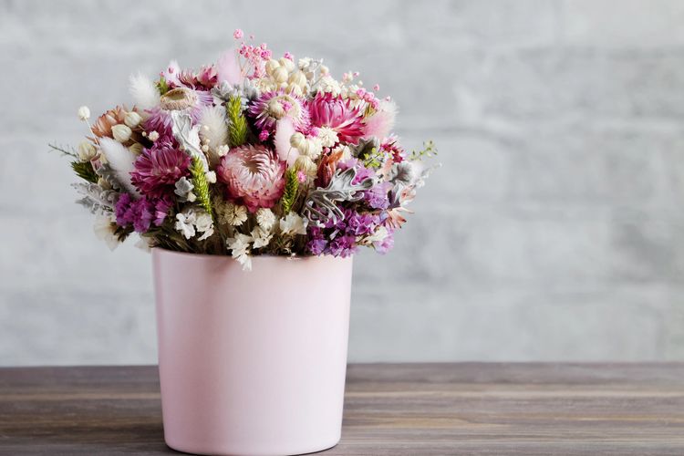 Pink pot filled with dried flowers on a wooden counter surface. 