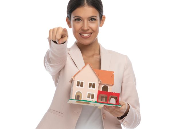 Smiling woman holding a model house and pointing forward.