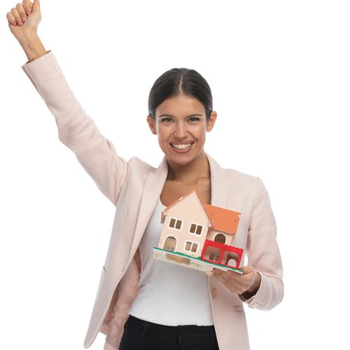 Happy woman holding a model house, celebrating with raised fist.
