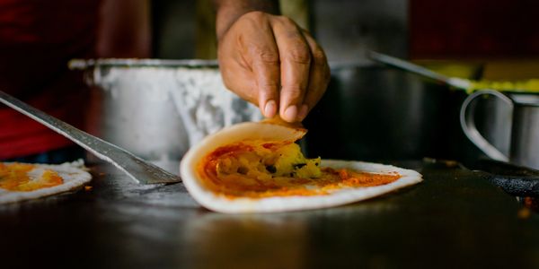 A hand folding a dosa filled with potato masala on a griddle.