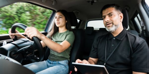 A young woman driving a car with an instructor beside her.