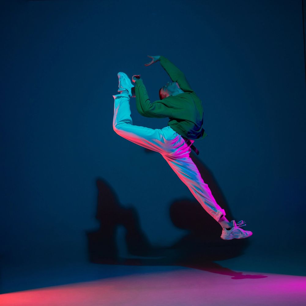 A dancer mid-air in a dramatic leap under colorful lighting.
