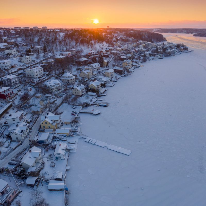 Sunset in winter over waterfront houses by lake Mälaren in Mälarhöjden outside Stockholm, Sweden.