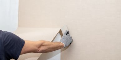 Person removing beige wallpaper from a wall.