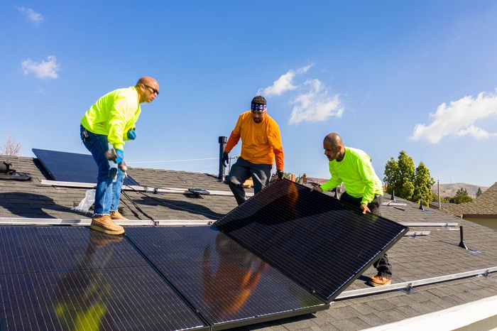 A technician installs solar panels on a rooftop under a clear sky.
