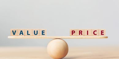 Wooden blocks spelling Value and Price balanced on a wooden seesaw.
