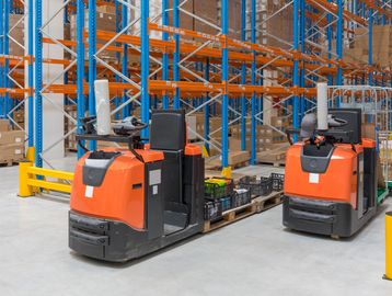 Two electric pallet jacks in a warehouse with blue and orange shelving.