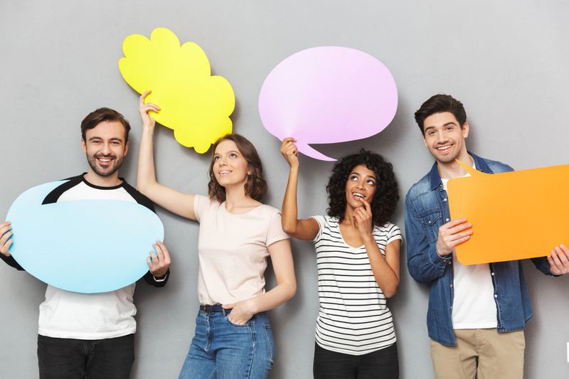 Image of emotional group of friends standing isolated over grey wall background holding speech and thoughtful bubbles.
