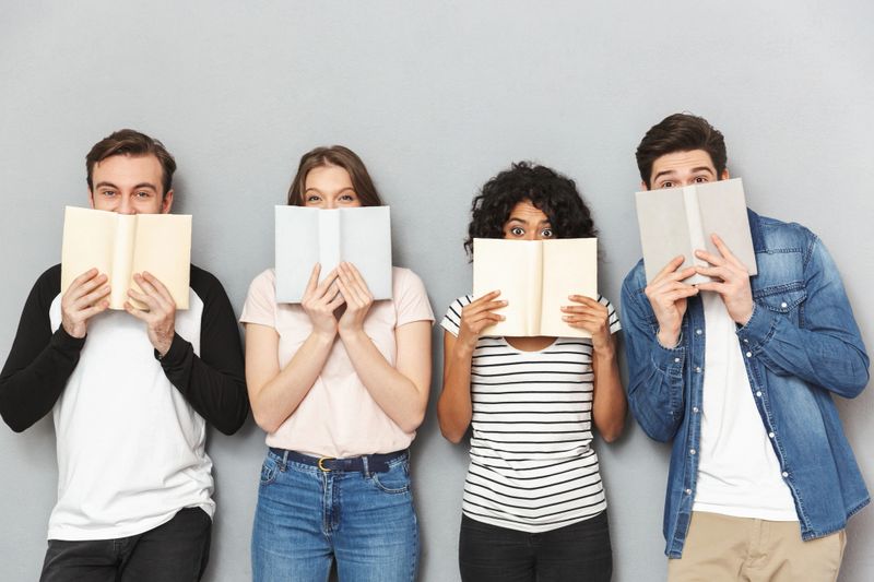 Group of excited young multiethnic friends holding books isolated over gray background