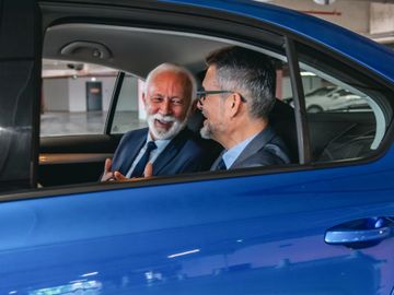 Two businessmen smiling and talking inside a blue car.