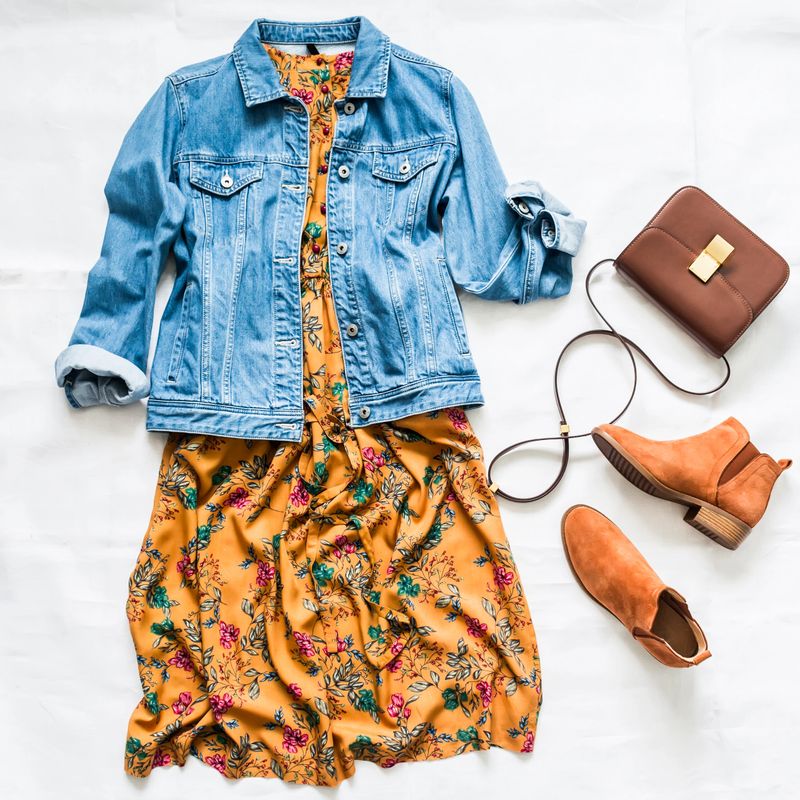Denim jacket, vintage floral print dress, suede red chelsea boots and leather bag on a light background, top view. Beauty fashion concept