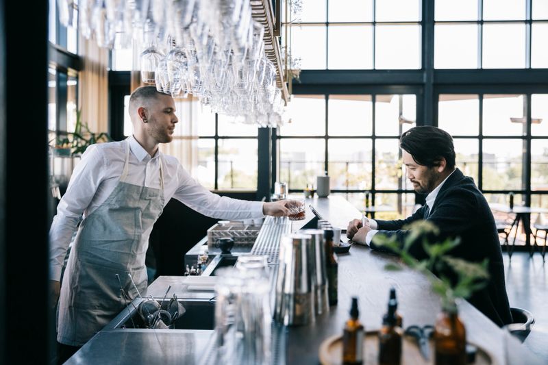 Waiter giving whiskey to the client at the airport bar