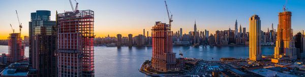 Sunset over a city skyline with construction cranes and river.