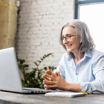 Older woman with glasses smiling during a video call on laptop.