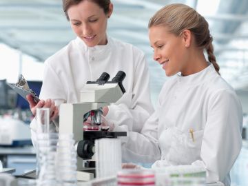 Two female scientists working with a microscope in a lab.